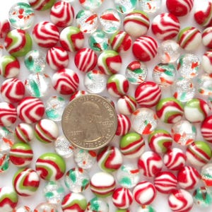 May include: A collection of glass marbles in various colors and designs. The marbles feature red and white stripes, green and white swirls, and clear glass with red and green flecks. A U.S. quarter is included for size reference.
