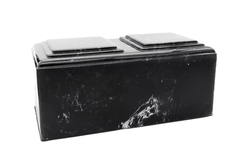 May include: A black marble cremation urn with two separate compartments. The urn has a smooth, polished finish and a rectangular shape.