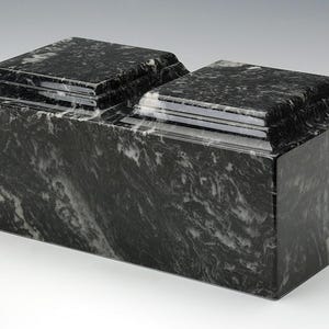 May include: A black and white marble cremation urn with a double-tiered design. The urn has a smooth, polished finish.