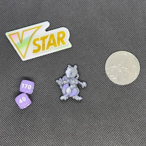 May include: A purple and white Pokemon character figurine, two purple dice with the numbers 40 and 170, a silver coin, and a VSTAR logo.