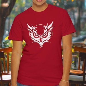 Peut inclure: T-shirt rouge avec un graphique de hibou stylisé blanc. Le hibou a une expression féroce avec de grands yeux et un bec pointu.