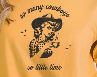 May include: A yellow t-shirt with a black and white graphic of a woman wearing a cowboy hat and holding a cup of coffee. The text on the shirt reads "so many cowboys so little time".