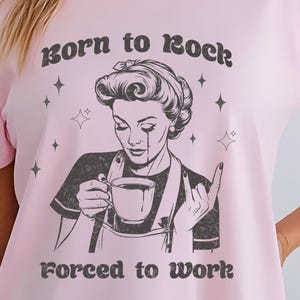 May include: Pink t-shirt with a black and white illustration of a woman holding a cup of coffee. The text "Born to Rock. Forced to Work." is printed on the shirt.