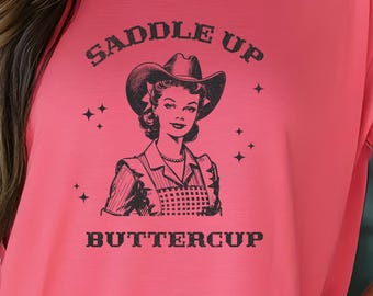 May include: A pink t-shirt with a graphic of a woman wearing a cowboy hat and the text "Saddle Up Buttercup".