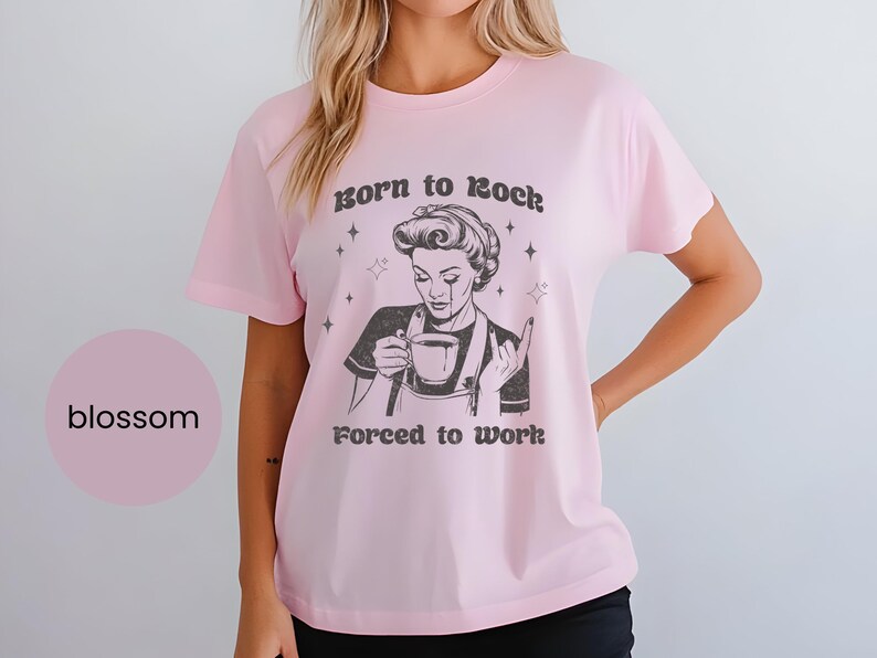 May include: Pink t-shirt with a black and white illustration of a woman holding a cup of coffee. The text "Born to Rock. Forced to Work." is printed on the shirt.