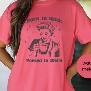May include: A pink t-shirt with a black and white illustration of a woman holding a cup of coffee. The text on the shirt reads "Born to Rock Forced to Work".