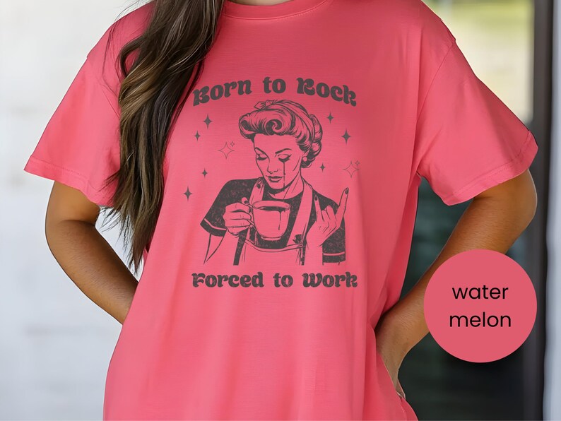May include: A pink t-shirt with a black and white illustration of a woman holding a cup of coffee. The text on the shirt reads "Born to Rock Forced to Work".