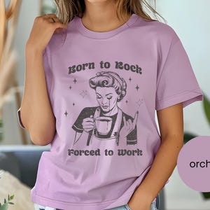 May include: A purple t-shirt with a graphic of a woman holding a cup of coffee and the text "Born to Rock Forced to Work".