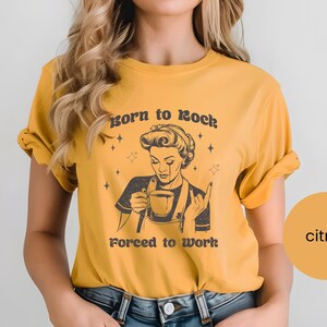May include: A yellow t-shirt with a retro-style illustration of a woman drinking coffee. The text on the shirt reads "Born to Rock Forced to Work".