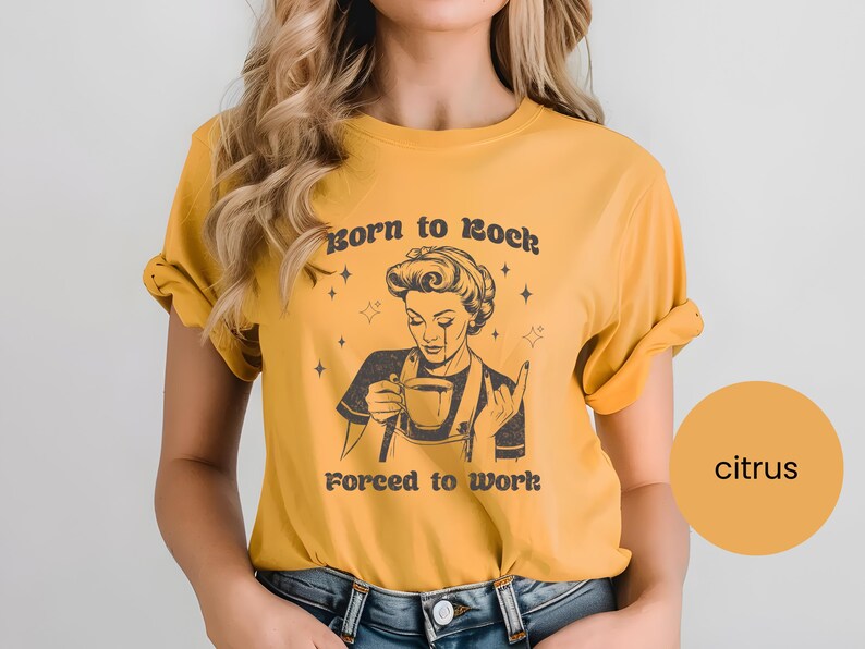 May include: A yellow t-shirt with a retro-style illustration of a woman drinking coffee. The text on the shirt reads "Born to Rock Forced to Work".