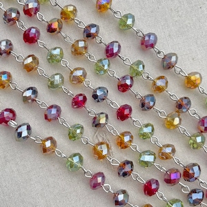 May include: A strand of faceted glass beads in shades of red, green, and gold, strung on a silver chain. The beads are all approximately the same size and shape, and they are arranged in a repeating pattern.