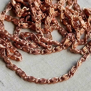 May include: A close-up of a copper chain with a detailed, intricate design. The chain is made of small, linked loops that create a delicate and elegant look.
