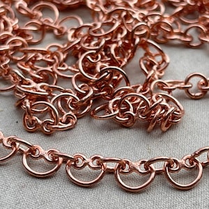 May include: A close-up of a copper chain with a delicate, intricate design. The chain is made of small, interconnected loops that create a flowing, elegant pattern.