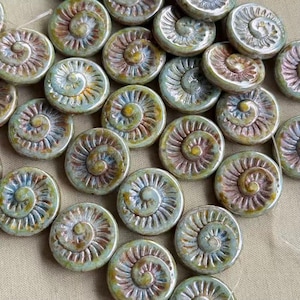 May include: A collection of round ceramic beads featuring a raised spiral pattern. Each bead displays a glossy glaze with blended tones of sage green, soft blue, and warm brown, creating a textured surface with a distinct, swirling relief design.