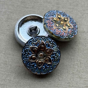 May include: Three round, decorative buttons with a blue and gold floral design. The buttons have a raised, textured surface and a shiny finish.