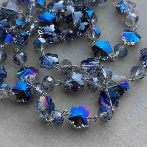 May include: A strand of iridescent blue and clear crystal beads with a silver chain. The beads are faceted and have a starburst shape.