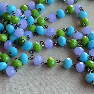 May include: Close-up of a beaded necklace with faceted beads in shades of light blue, green, and lavender. The beads are strung together with silver-colored metal links, creating a delicate and colorful accessory.