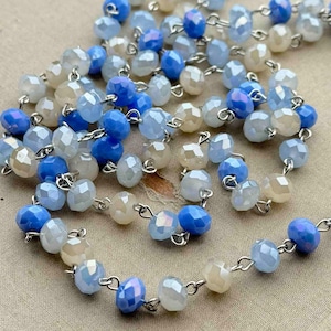 May include: A strand of blue and white crystal beads strung on a silver chain. The beads are faceted and have a subtle iridescent sheen.