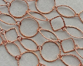 May include: A long chain necklace made of rose gold metal. The chain is made of interconnected oval, round, and square links. The links have a textured, hammered finish.