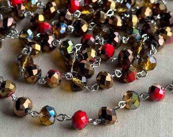 May include: A strand of brown and red faceted glass beads strung on a silver chain. The beads are iridescent and have a sparkly finish.