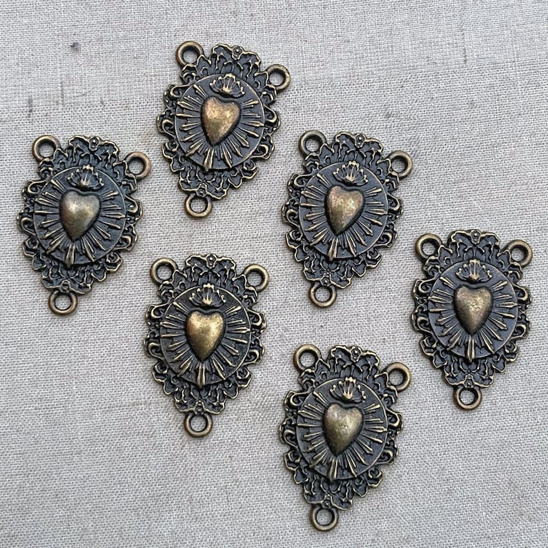 Puede incluir: Seis encantos de metal dorado antiguo con un dise&ntilde;o de coraz&oacute;n. Cada encanto presenta un coraz&oacute;n con una corona y rayos de luz. Los encantos tienen tres bucles para sujetar a joyas u otras artesan&iacute;as.