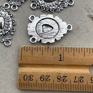 May include: Silver-toned metal charm with a heart design and three jump rings. The charm is approximately 1 inch in diameter and is measured against a ruler.