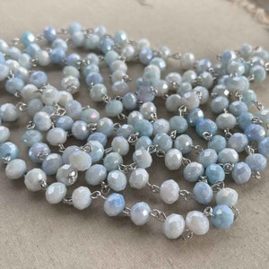 May include: A strand of light blue and white faceted glass beads strung on a silver chain. The beads are iridescent and have a subtle shimmer.