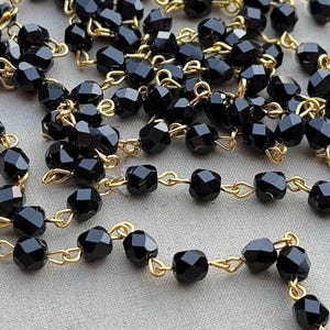 May include: A black beaded chain with gold links. The beads are faceted and have a dark, glossy finish.