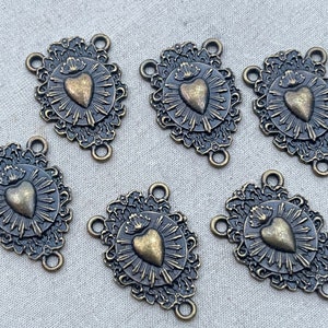 Puede incluir: Seis encantos de metal de color dorado antiguo con un coraz&oacute;n con una corona y un dise&ntilde;o de sol. Cada encanto tiene tres bucles para sujetar a joyas u otras manualidades.