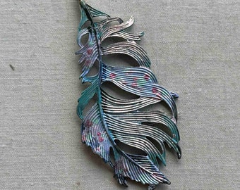 May include: A silver and blue metal feather with a detailed design and red accents. The feather is a decorative piece with a vintage look.