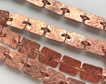 May include: A copper chain made of square links with a textured surface. The chain is made of multiple links connected together.
