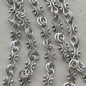 Puede incluir: Primer plano de un collar de cadena de plata con un dise&ntilde;o delicado e intrincado. La cadena presenta un patr&oacute;n repetitivo de peque&ntilde;as cuentas redondas y eslabones curvos.