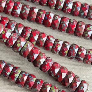 May include: Close-up of several strands of faceted beads. The beads are a deep red color with a speckled pattern of green, yellow, and white. The beads have a geometric shape and are strung together, creating a textured surface.