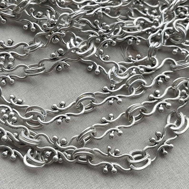 Puede incluir: Un collar de cadena de plata con un dise&ntilde;o delicado e intrincado que presenta peque&ntilde;as cuentas redondas y eslabones curvos.