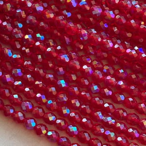 May include: Close-up of a collection of faceted red beads. The beads have an iridescent sheen, reflecting multiple colors. The beads are strung together, creating a textured surface. Ideal for jewelry making and crafting.