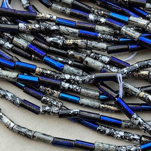 May include: A strand of black and blue glass beads with silver and gold flecks. The beads are cylindrical and have a speckled, textured surface.