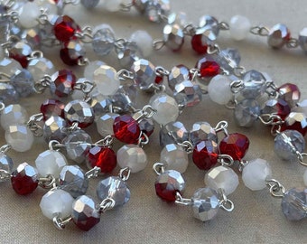 May include: A strand of beaded garland with red, white, and silver beads. The beads are connected by a silver chain.