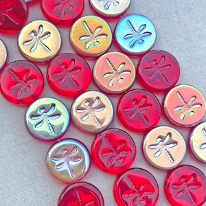 May include: Assortment of round glass beads with dragonfly designs. The beads are in shades of red, gold, and blue with iridescent finishes.
