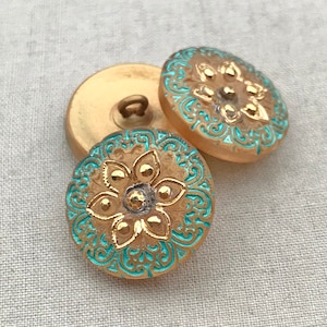 May include: Two gold-colored buttons with a turquoise blue floral design. The buttons have a raised flower design with gold accents.