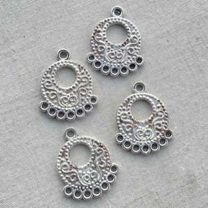 May include: Four silver-toned metal pendant charms with a circular design and intricate filigree details. Each charm has a small loop at the top for attaching to jewelry or other crafts.