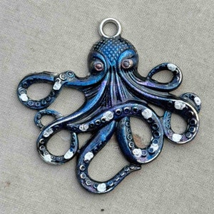 May include: A dark blue octopus pendant with white accents. The octopus has eight tentacles and a detailed head with eyes. The pendant has a loop at the top for hanging.