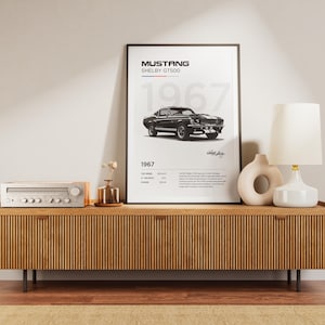 May include: A black and white poster of a 1967 Ford Mustang Shelby GT500 with the text "Mustang Shelby GT500 1967" on a wooden shelf with a stereo and a lamp.