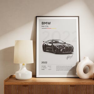 May include: A black and white poster featuring a black BMW M4 CSL with the text "BMW M4 CSL 2022" and a signature at the bottom.