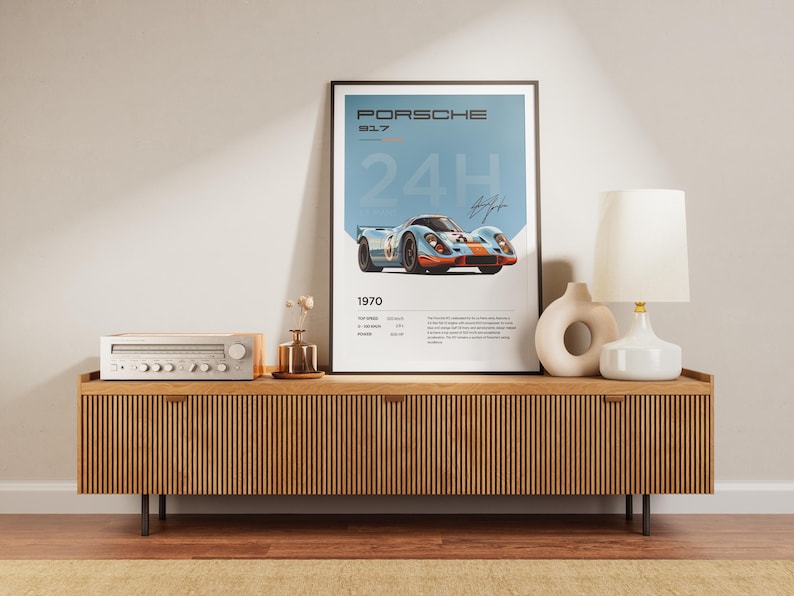 K&ouml;nnte beinhalten: Ein gerahmtes Poster mit blauem Hintergrund, auf dem ein Vintage-Porsche 917-Rennwagen abgebildet ist. Das Poster tr&auml;gt den Text "PORSCHE 917 24H 1970". Das Poster ist auf einem Holzregal mit einer Stereoanlage und einer Lampe ausgestellt.