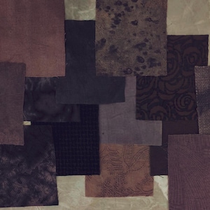 May include: A collection of fabric swatches in various shades of brown, purple, and black. The swatches have different textures and patterns, including solid colors, floral designs, and speckled effects. The arrangement is on a neutral background.