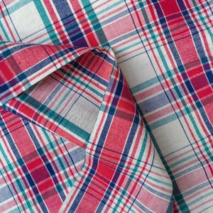 May include: Red, white, and blue plaid fabric with a folded corner. The fabric has a woven texture and a checkered pattern.