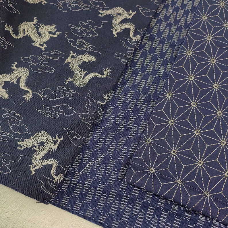 May include: Three different fabric swatches in a dark blue color with white patterns. The first swatch has a repeating pattern of dragons and clouds. The second swatch has a repeating pattern of small white dots. The third swatch has a repeating pattern of geometric shapes.