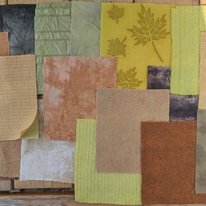 May include: Assortment of fabric swatches in various shades of green, brown, and beige. The fabric swatches are arranged in a grid pattern on a wooden surface. Some of the fabrics have a textured or patterned surface.
