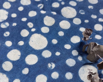 May include: A blue fabric with a white polka dot pattern. The fabric is textured and has a slightly distressed look. A sprig of dried eucalyptus leaves is resting on the fabric.