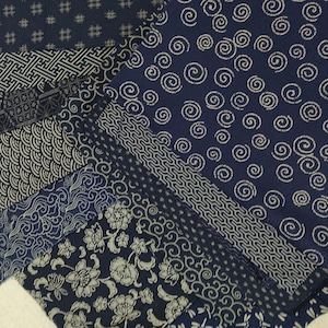 Puede incluir: Una colección de muestras de tela azul índigo con varios patrones blancos, incluyendo espirales, formas geométricas y diseños florales.